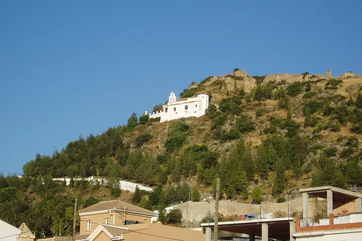 En primer plano, una iglesia blanca en una colina rodeada de árboles
