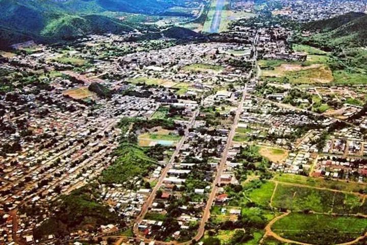 En primer plano, una avenida principal con edificios y casas a ambos lados, rodeada de montañas