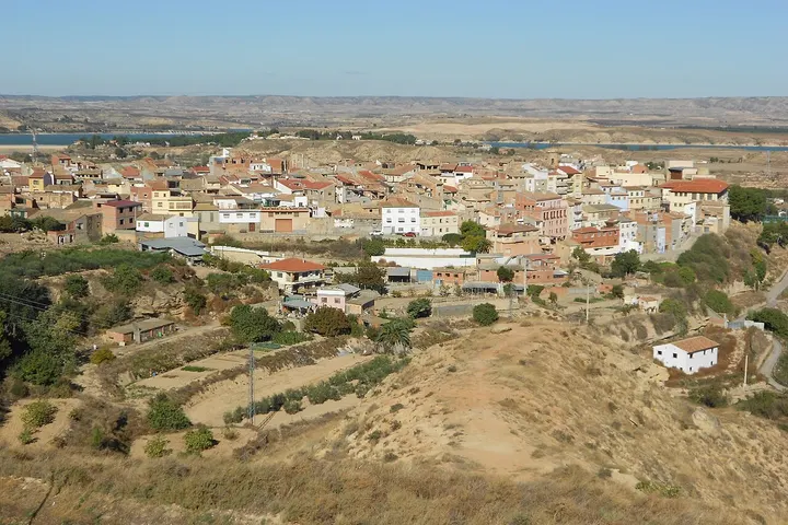 En primer plano, se ve un terreno seco con arbustos y una casa blanca