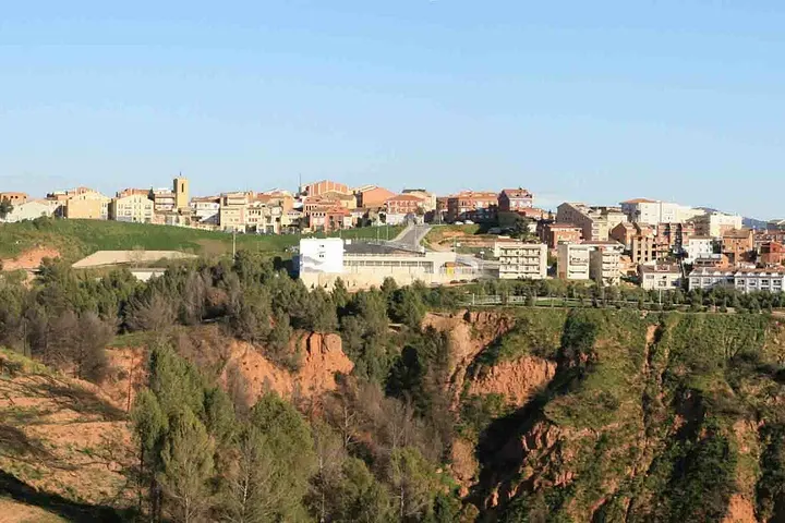 En primer plano, una profunda garganta se abre, rodeada de árboles y rocas rojas