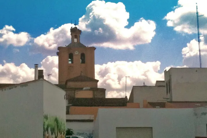 En primer plano, una torre de iglesia con reloj y campanas