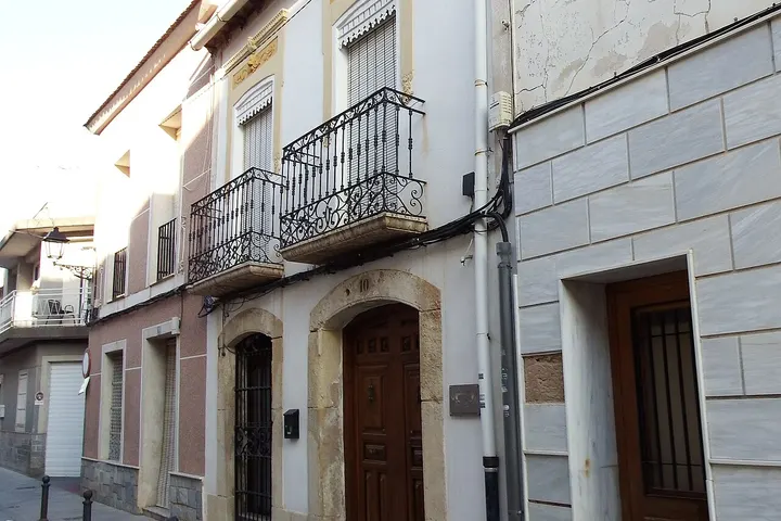 En primer plano, dos balcones con barandillas de hierro forjado adornan una casa de dos pisos con puertas de madera