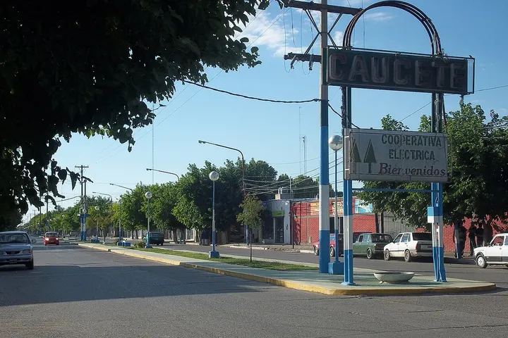 En primer plano, una señal de bienvenida con el nombre de un pueblo, con una cooperativa eléctrica