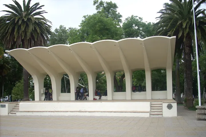 Un edificio blanco con una estructura de techo en forma de concha, rodeado de palmeras y árboles