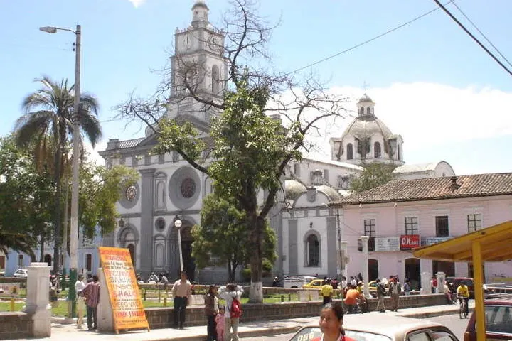 En primer plano, una iglesia blanca con torres y un edificio rosa con un cartel rojo