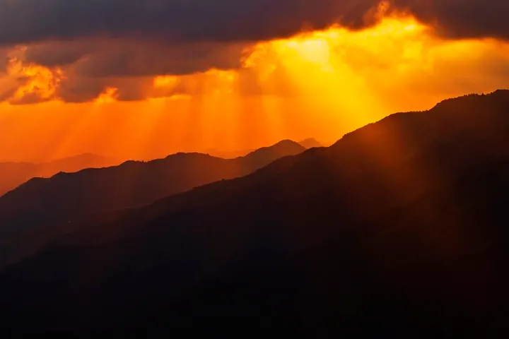 En primer plano, se ve un atardecer con una montaña en el horizonte