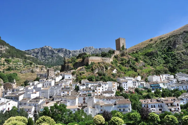 En primer plano, se aprecia una torre de piedra, rodeada de casas blancas y árboles