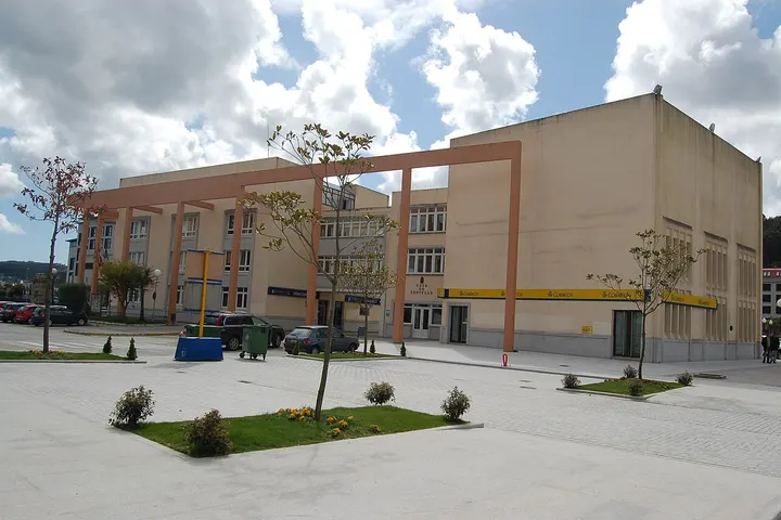 En primer plano, una gran escuela con un parque con árboles y flores