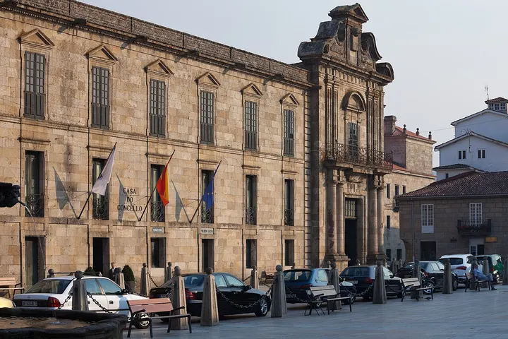 En primer plano, una gran edificación de piedra con banderas al frente