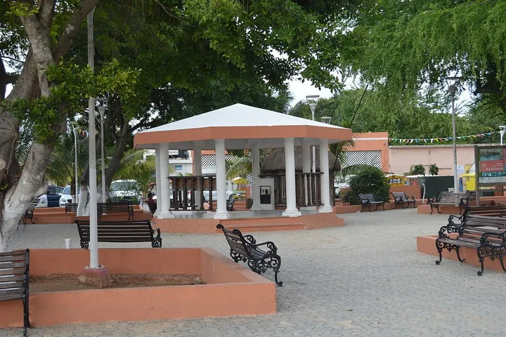 En primer plano, un kiosco de estilo clásico con columnas blancas y un techo de color rojo