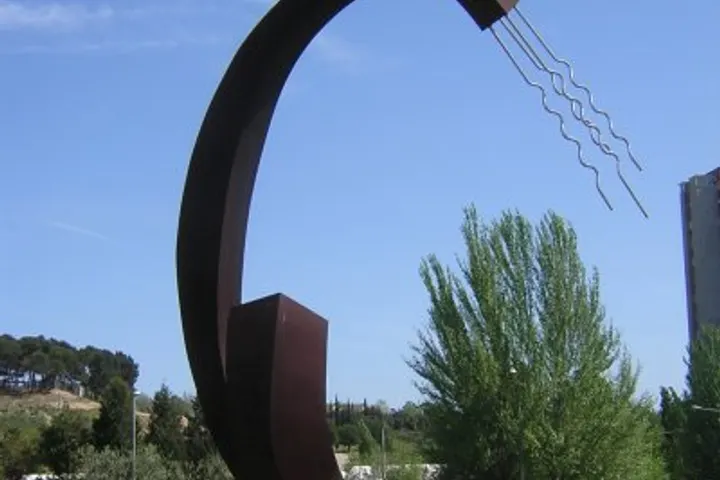 En primer plano, un monumento de hierro con forma de arco, con una figura en el centro