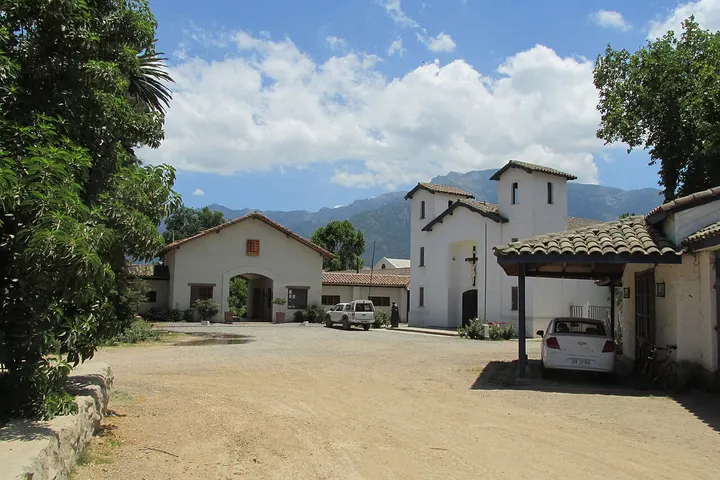 Capilla blanca y edificios de una escuela agrícola con montañas y cielo nuboso al fondo