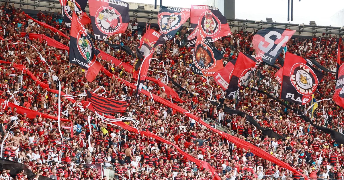 Adeptos com bandeiras vermelhas e pretas enchem a bancada de um estádio