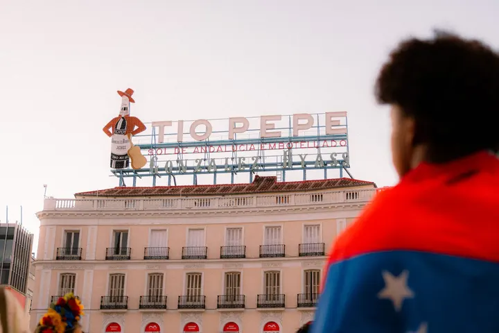 Cartel luminoso de Tío Pepe en la Puerta del Sol visto tras una persona con una bandera al hombro