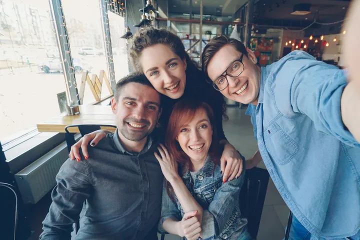 Cuatro amigos sonrientes se abrazan para una selfie en una cafetería