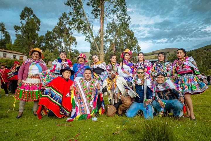 Grupo con trajes tradicionales de colores vivos posa sobre la hierba ante un bosque de eucaliptos