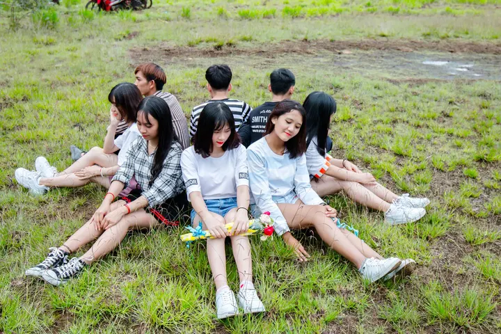 Un grupo de ocho personas, posiblemente jóvenes, se sientan en una pradera, con sus espaldas unidas, mirando hacia la cámara