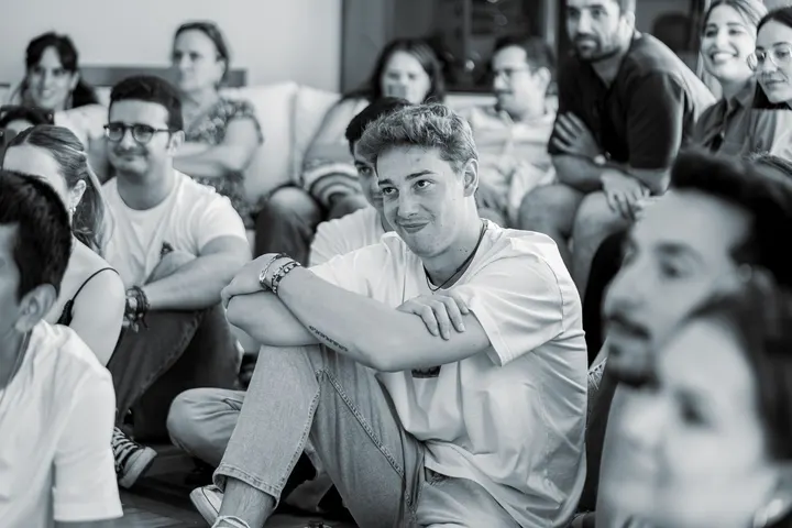 Un grupo de jóvenes sentados en el suelo, en una habitación, atentos a algo