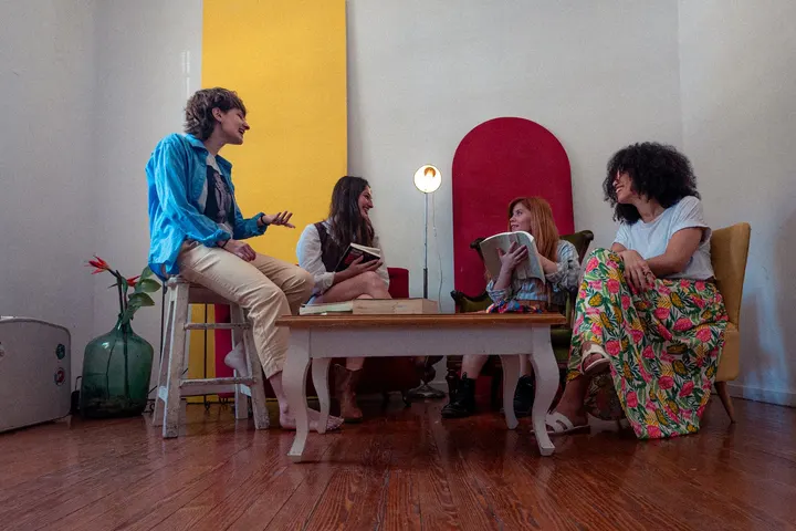 Cuatro personas sentadas alrededor de una mesa, en una habitación con paredes blancas y un suelo de madera