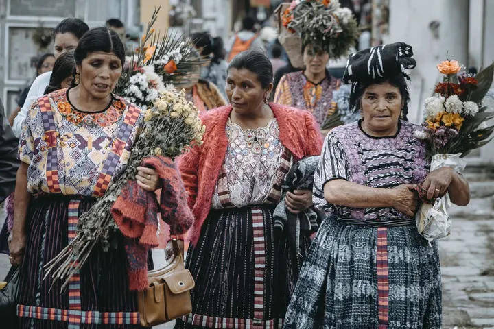 Mujeres indígenas de México portan flores y caminan por una calle
