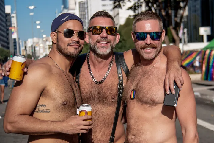 Tres hombres, posiblemente en un evento del orgullo gay, están bebiendo cerveza en un día soleado