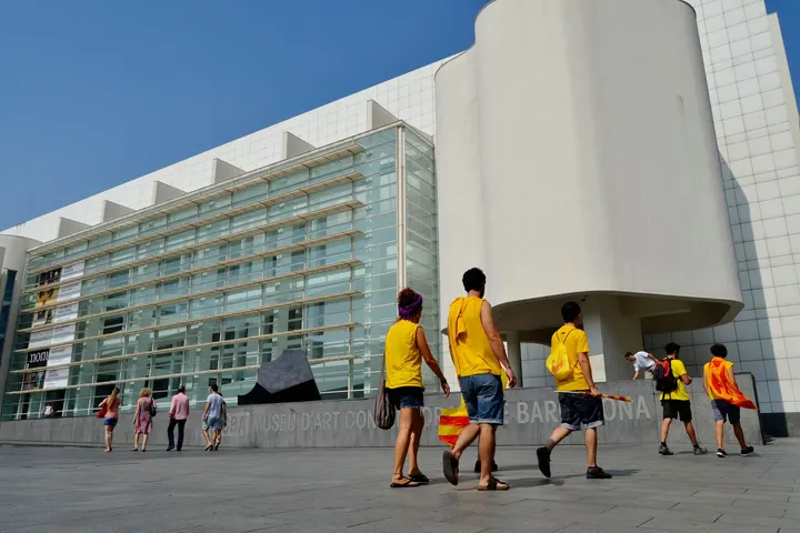 En la plaza del Museo de Arte Contemporáneo de Barcelona, personas con camisetas amarillas caminan hacia el edificio