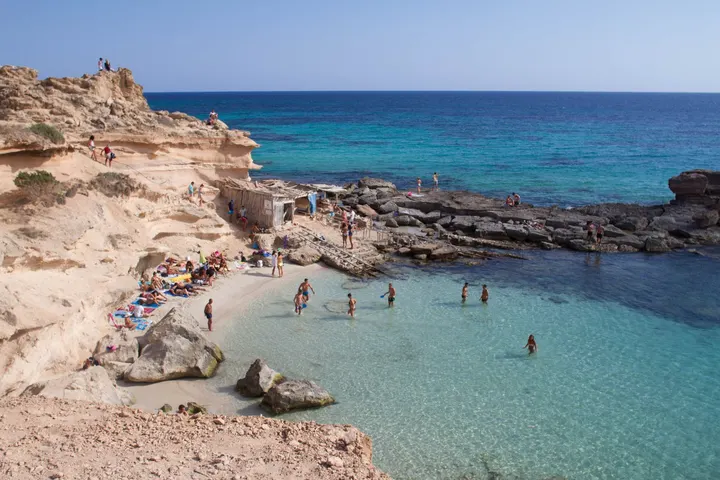 Cala de aguas turquesas con bañistas entre rocas calizas en las Illes Balears