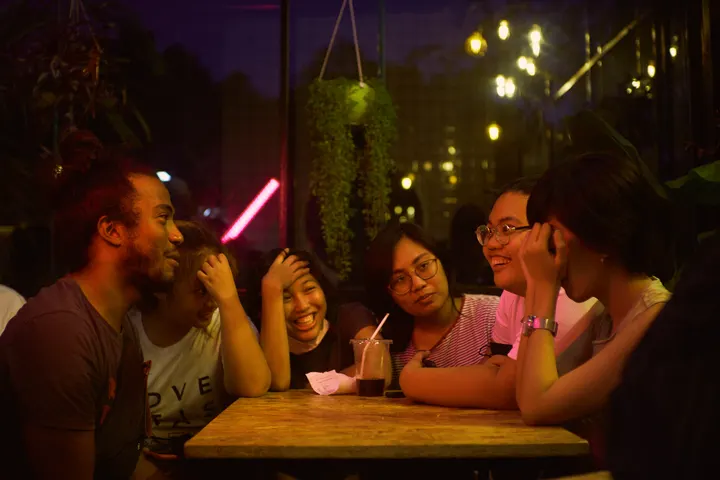 Un grupo de cinco personas, sentadas alrededor de una mesa, en un bar, en una noche oscura