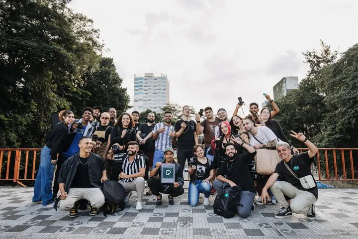 Un grupo de personas, posando para una foto, en un parque con árboles y edificios en el fondo