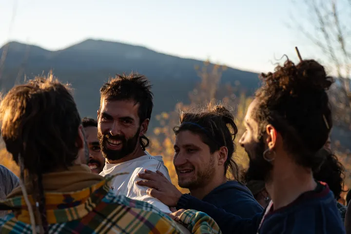Un grupo de hombres con largas barbas y el cabello recogido, están en el campo, en un paisaje montañoso