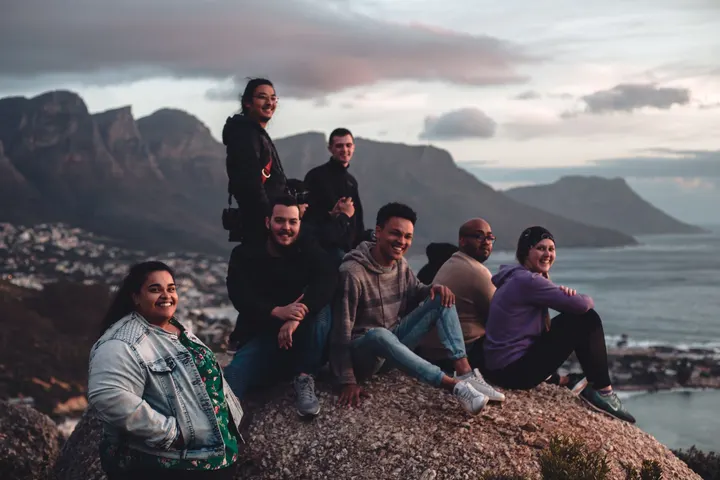 Grupo de amigos posa sobre unas rocas frente al mar y las montañas al atardecer