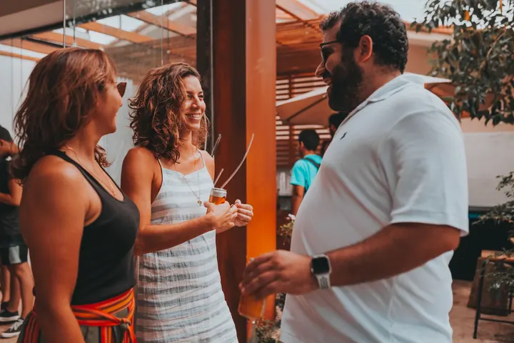 Dos mujeres y un hombre están en un patio, conversando y tomando bebidas