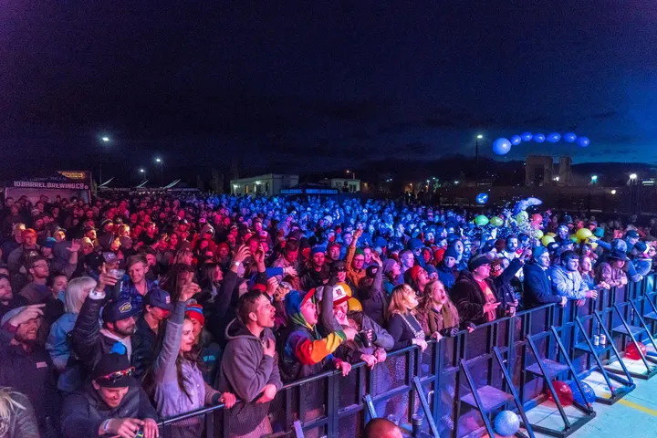Un grupo de personas, que parecen estar en una fiesta, están en una plaza, cantando y bailando