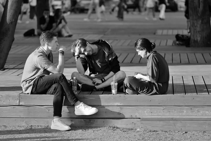 Tres jóvenes conversan sentados en unos escalones en blanco y negro